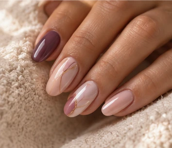 Nude almond nails with one deep plum accent nail and delicate gold line details